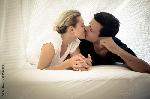 Caucasian couple kissing under the sheets on the bed at home in the bedroom - intimate lifestyle for young people in love - romantic valentine's day concept picture for attractive man and woman