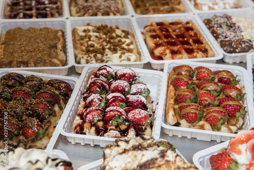 Belgian Waffles With Fruits and Toppings are being sold at a restaurant. The closeup image of the foods being sold looks delicious. They are arranged in a proper order for display.
