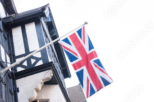 Closeup of a Birtish Flag or Union Jack is seen hanging from a building. The glass windows along with the clear bright sky is also seen in the picture. photo