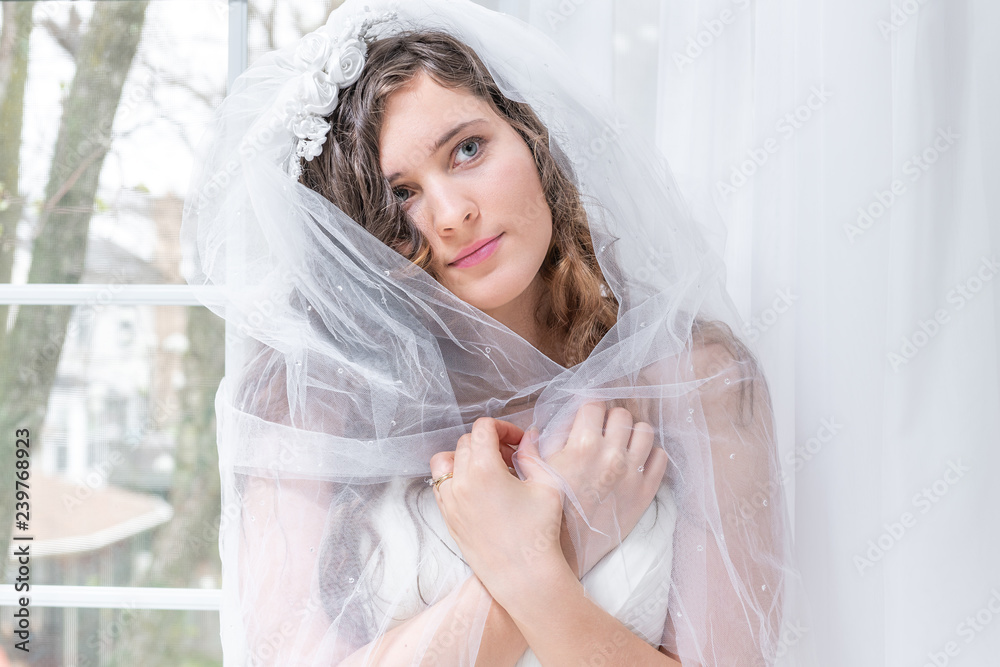 Closeup portrait of young female person, woman, bride in wedding dress,  holding, wrapping, covering around shoulders with wrapped veil, by window,  white curtains, looking up, in engagement ring Stock Photo | Adobe