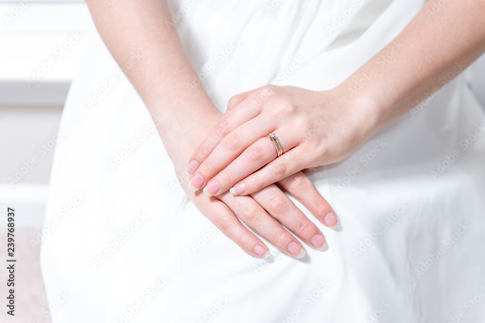 Closeup of hands of young female person, woman, bride in wedding dress, sitting by window, white curtains with engagement diamond ring on finger of hands Closeup of hands of young female person, woman, bride in wedding dress, sitting by window, white curtains with engagement diamond ring on finger of hands