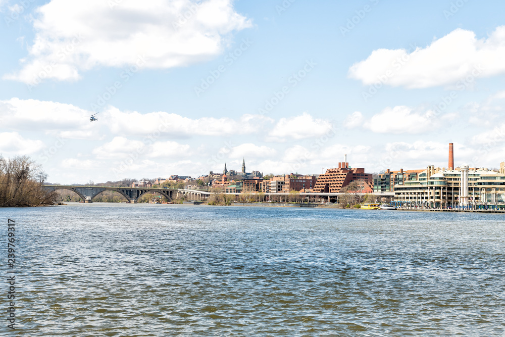 Cityscape, skyline view of Potomac river, Georgetown waterfront park in Washington, DC, District of Columbia, water waves, helicopter flying on sunny spring day, Whitehurst freeway, blue sky ,clouds