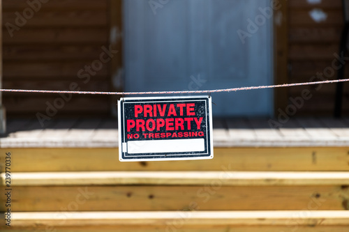 Private property no trespassing sign hanging on rope, wire outside, outdoors on street by house, home building with entrance, steps, stairs, staircase, door, porch