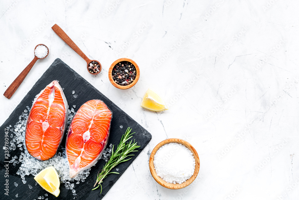 Cooking salmon steak from raw fish on black plate with spices, rosemary, lemon and salt on marble restaurant kitchen table background top view copy space Cooking salmon steak from raw fish on black plate with spices, rosemary, lemon and salt on marble restaurant kitchen table background top view copy space
