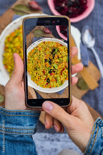 Phone food photo. Hands take smartphone food photography of Italian risotto rice or vegetables pilaf, colored pilau for social networks or blogging. Vegan, vegetarian healthy food 