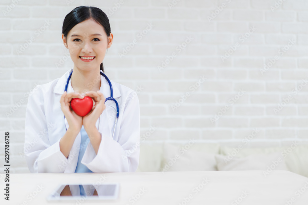 Young woman doctor holding a red heart, standing on brick wall background Young woman doctor holding a red heart, standing on brick wall background