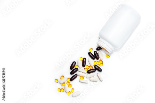 scattered tablets of vitamins spilling from white bottle with copy space. benefits of taking vitamins concept. dietary supplements abuse concept. isolated bank with tablets. 