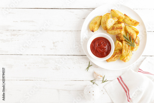 Potato baked and tomato ketchup on white plate, wooden background, top view