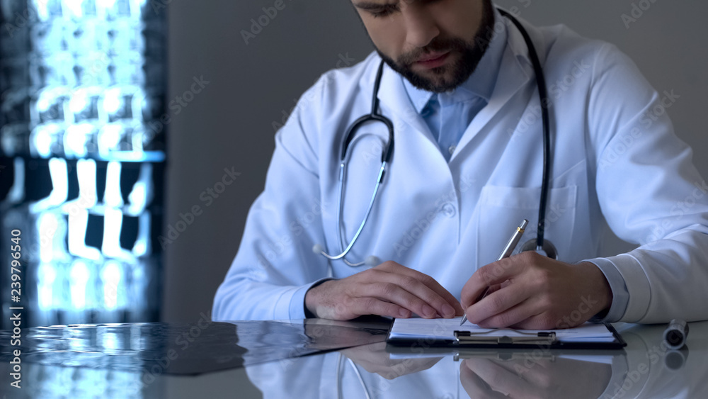 Experienced doctor examining x-ray and writing diagnosis in medical form, health Experienced doctor examining x-ray and writing diagnosis in medical form, health