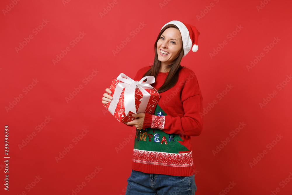 Stunning merry young Santa girl in knitted sweater, Christmas hat hold red box with gift, present isolated on red background. Happy New Year 2019 celebration holiday party concept. Mock up copy space. Stunning merry young Santa girl in knitted sweater, Christmas hat hold red box with gift, present isolated on red background. Happy New Year 2019 celebration holiday party concept. Mock up copy space.