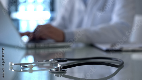Professional doctor working on laptop in lab, stethoscope on table, medicine