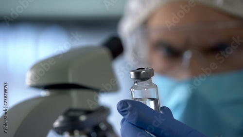 Scientist going to check injection bottle with new vaccine under microscope