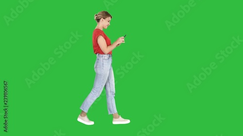 Beautiful young woman walking and reading text message on her mobile phone on a Green Screen, Chroma Key.