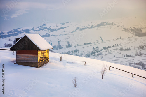 outskirts of the village on the hill. woodshed behind the wooden fence on a snowy slope. peaks of the distant mountain ridge in clouds. wonderful winter tale in gorgeous light © Pellinni