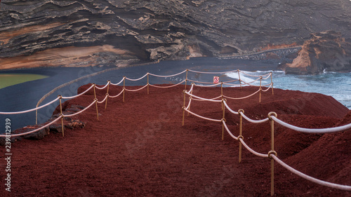 Red gravel foot path bordered with white rope in an amazing volcanic landscape with a green lake and a black sand beach. Green Lagoon (El Lago Verde) at El Golfo, Lanzarote, Canary Islands, Spain. photo