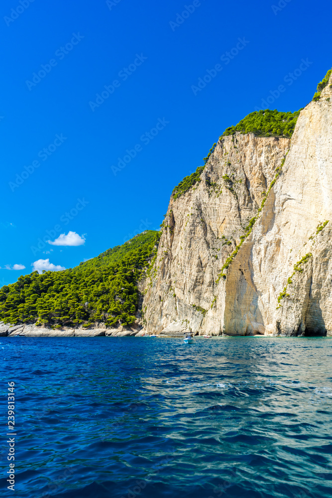 Greece, Zakynthos, Giant white chalk cliff covered by green trees from perfect blue ocean water