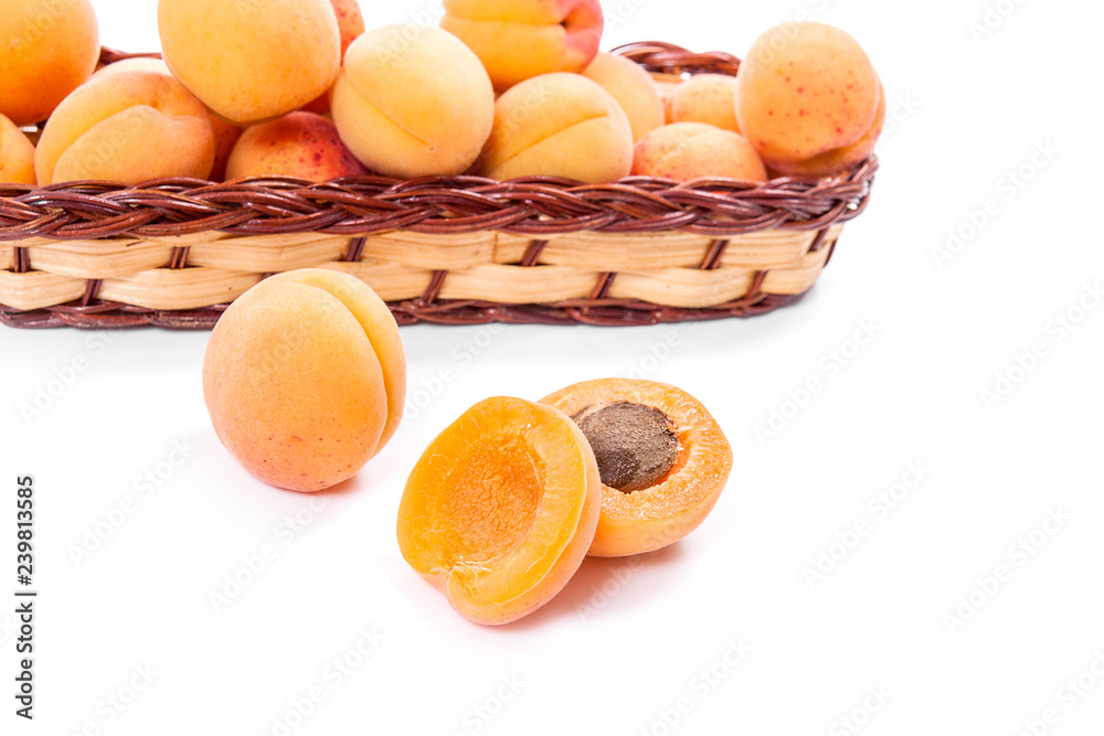 Several of harvested apricots in basket with whole and halved apricots on white background..