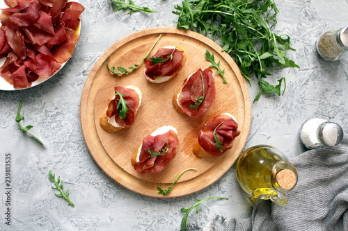 Canape or crostini with toasted baguette, light cheese, bresaola and arugula on wooden board. Diet food. Iron food.