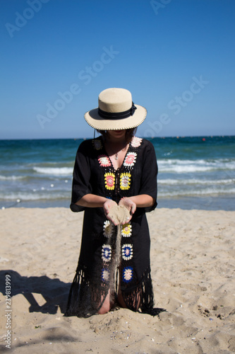 Sand falling from the woman's hand. Beautiful young woman in the hat on the beach with sand in her hand.