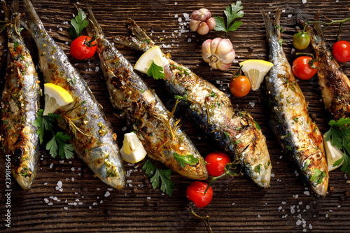 Grilled sardines with addition of fresh herbs, lemon and spices on a wooden background, top view. Grilled seafood, barbecue 