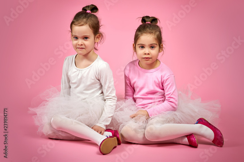 two cute little girls in white tulle skirts on a pink background
