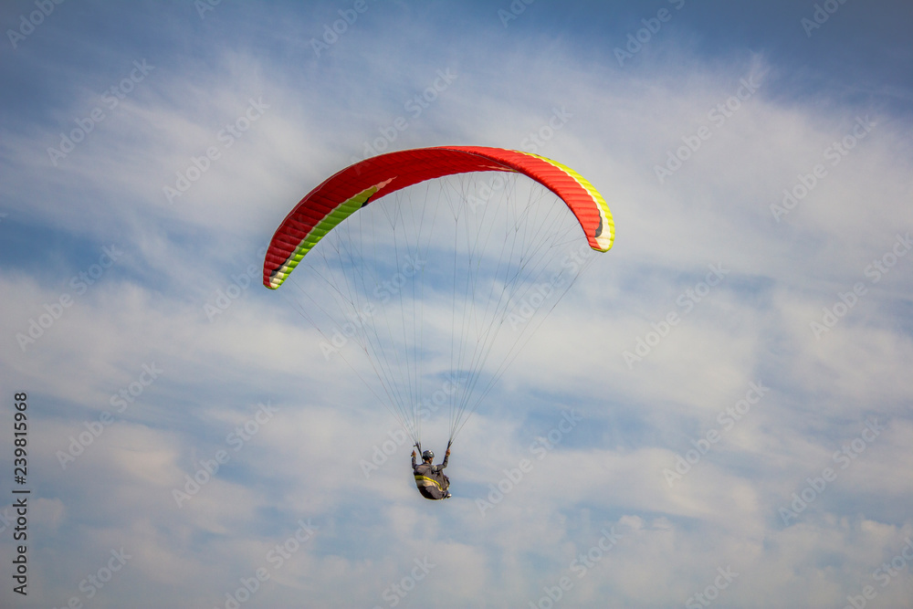 a paraglider on a red with yellow stripes paraglider flies in a blue sky with white clouds a paraglider on a red with yellow stripes paraglider flies in a blue sky with white clouds