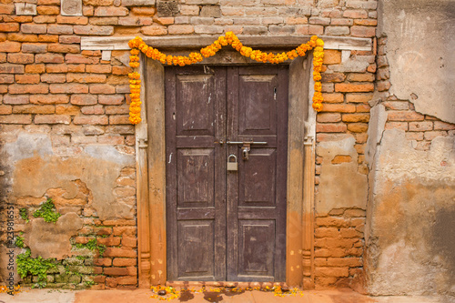 an old brown wooden door with a padlock in a damaged red brick wall, decorated with a garland of flowers for Diwali