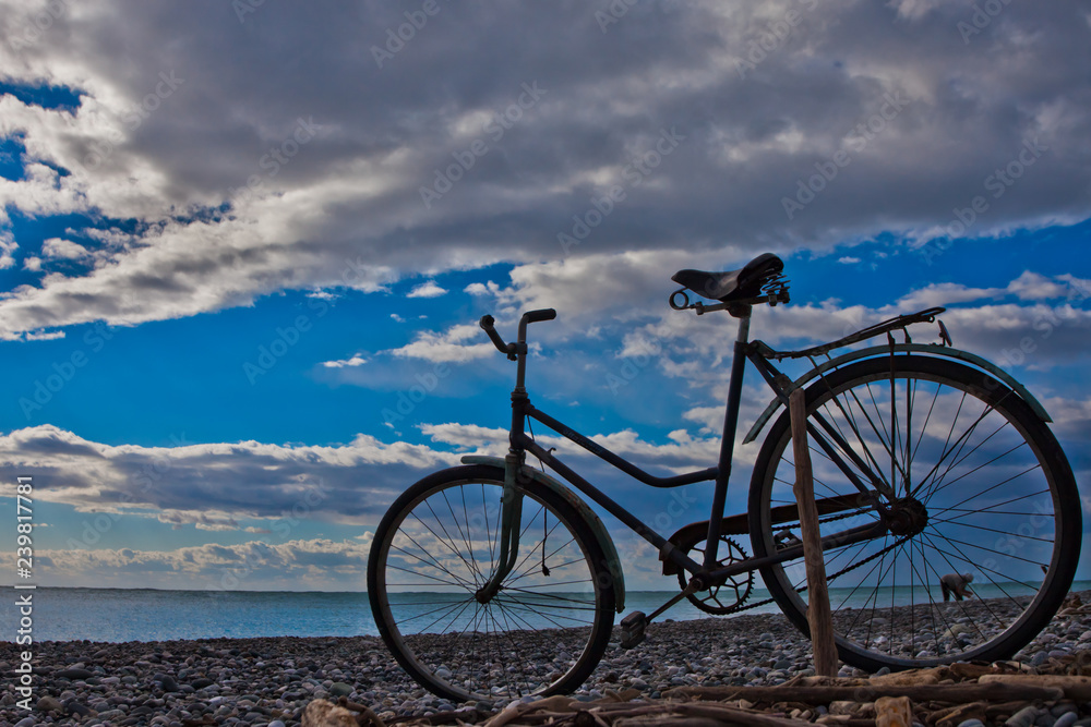 Fototapeta premium Classic (old) bicycle by the sea, blue sky with clouds, contrasting silhouette of a bicycle