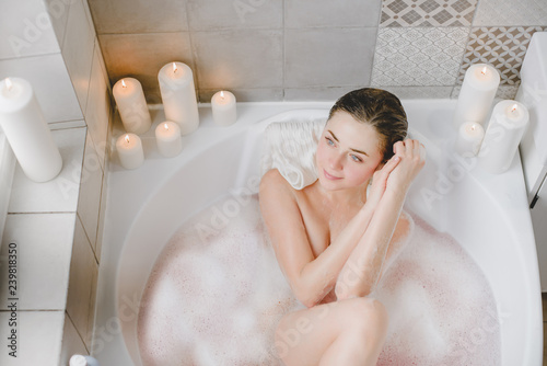 Young woman relaxes in a hot bath full of foam.