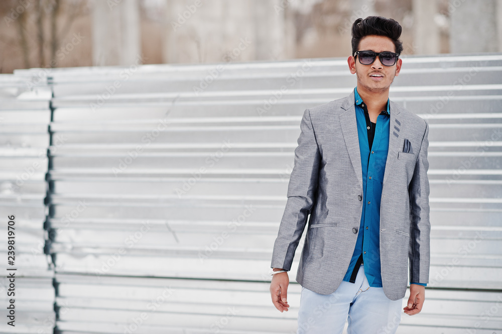 Casual young indian man in silver jacket and sunglasses posed against steel background. Casual young indian man in silver jacket and sunglasses posed against steel background.