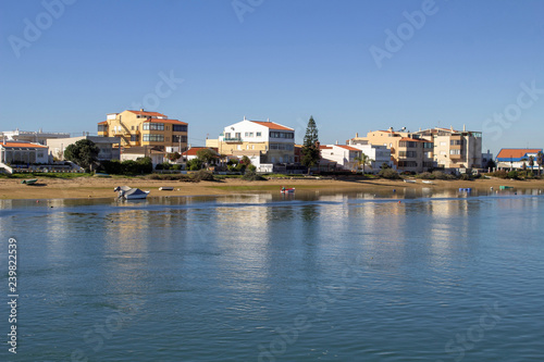 The beach on the Ria Formosa Lagoon side of Faro Island, Faro Portugal with small boats moored in the lagoon and appartment buildings in the background.
