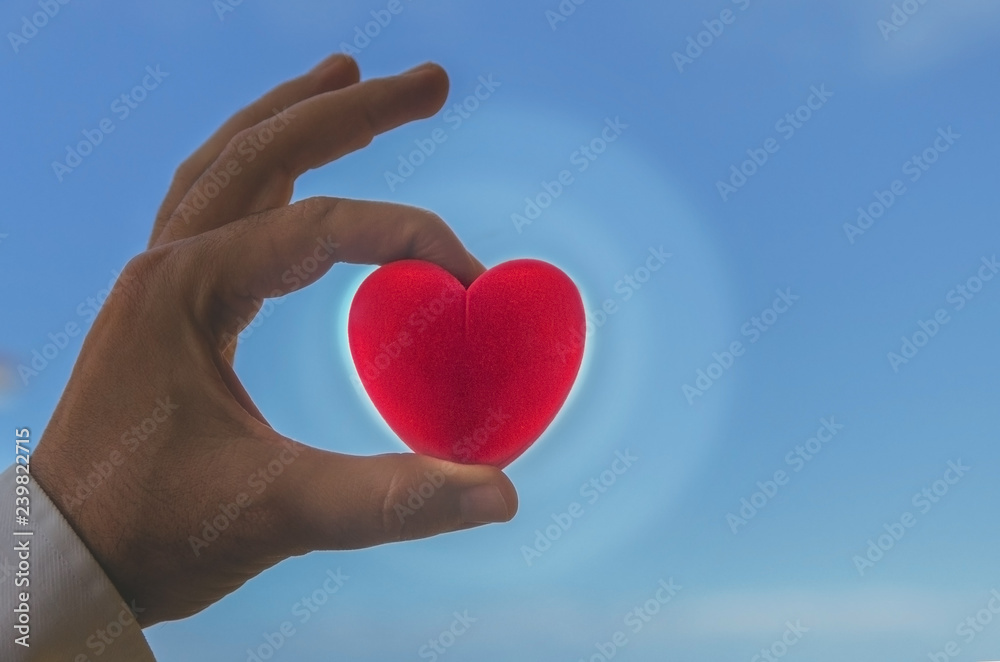 Obraz premium Man holding glowing red heart against blue sky . Help and donation concept.