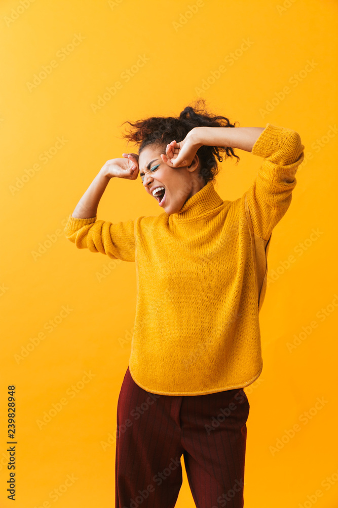 Portrait of pretty african american woman with afro hairstyle rejoicing and dancing, isolated over yellow background Portrait of pretty african american woman with afro hairstyle rejoicing and dancing, isolated over yellow background