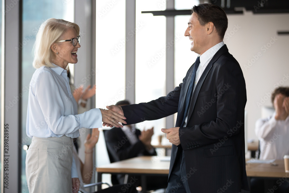 Middle aged excited employee getting reward shake hands with company boss. Executive manager congratulates best worker of the month handshaking with happy experienced colleague standing in coworking Middle aged excited employee getting reward shake hands with company boss. Executive manager congratulates best worker of the month handshaking with happy experienced colleague standing in coworking