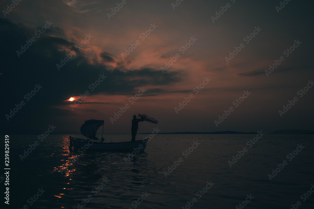 A fisherman tries to catch fish in sunset