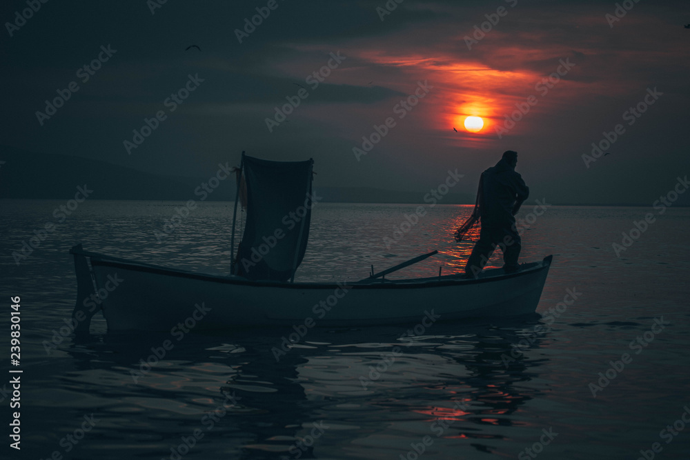 Naklejka premium Sun goes down while fisherman throws his fishnet to collect fishes