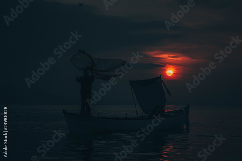 Sun goes down while fisherman throws his fishnet to collect fishes