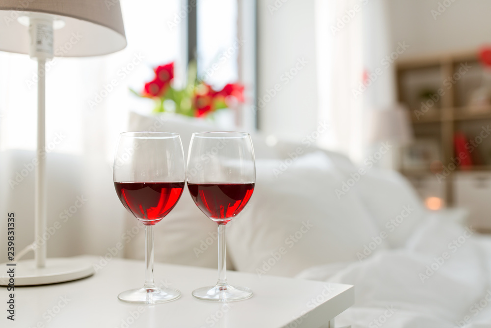 valentines day and romantic concept - two glasses of red wine on bedroom nightstand at home valentines day and romantic concept - two glasses of red wine on bedroom nightstand at home