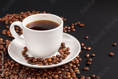 White Cup of strong coffee in roasted coffee beans  on a solid black background  foreground  close-up