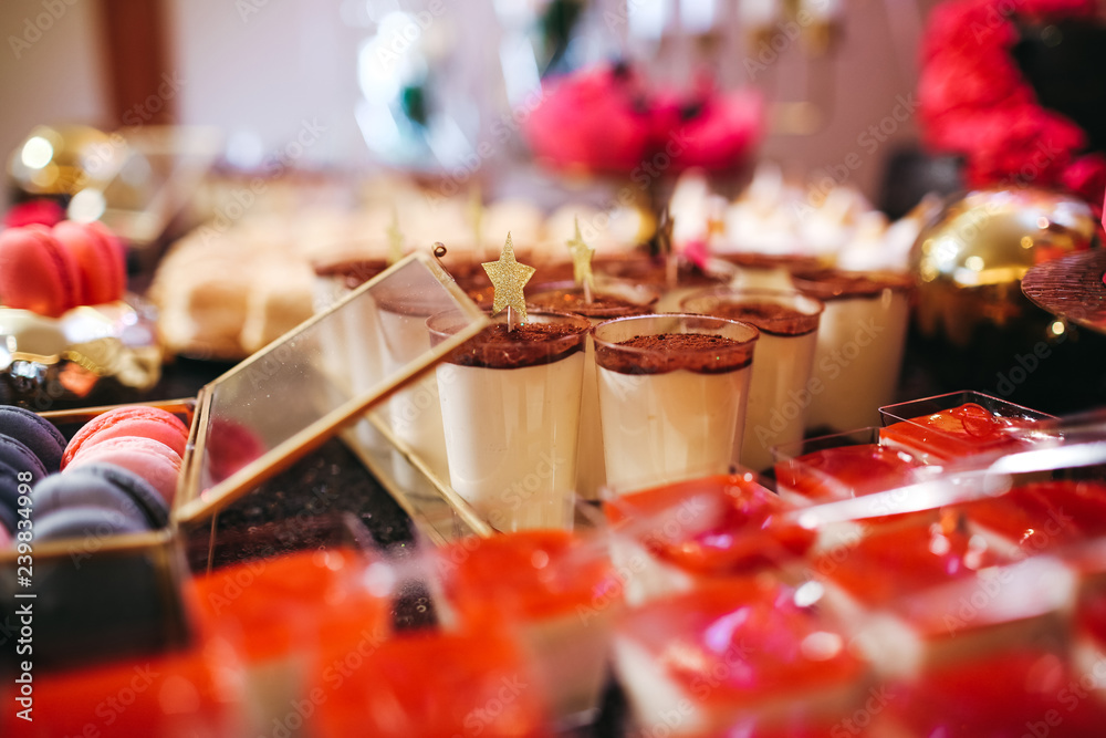 Candy bar table set. Cookies, eclairs, macaroons, fruits, cream and layered cakes. Black, golden and red colours.