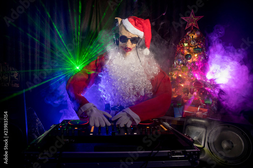 Dj Santa Claus at Christmas with glasses and snow mix on New Year's Eve event in the rays of light.