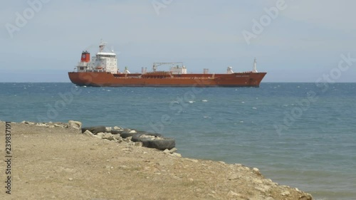 A brick red ship sailing in sea, view from the beach 
