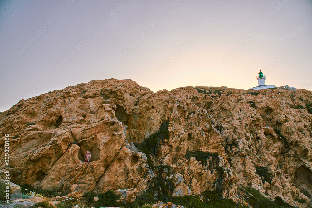 A tourist girl hiding in natural rock formation under the Pietra lighthouse in Corsica