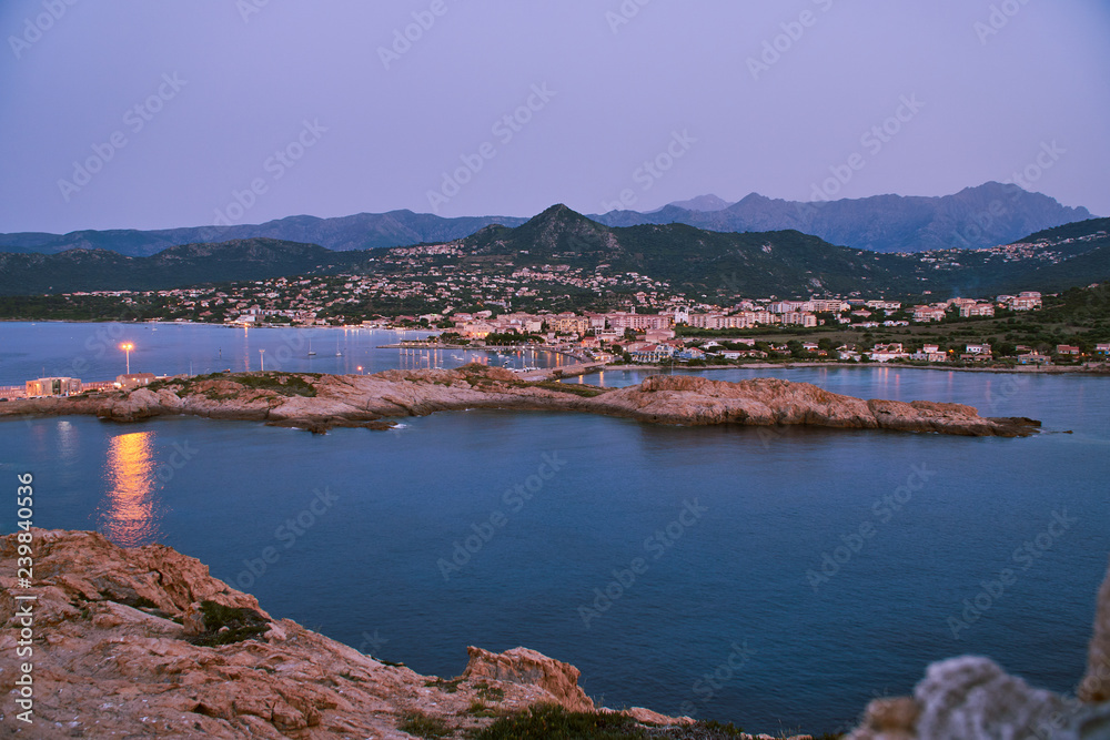 City of Ille Rouse in the evening with mountains in the background and sea in the foreground in Corsica