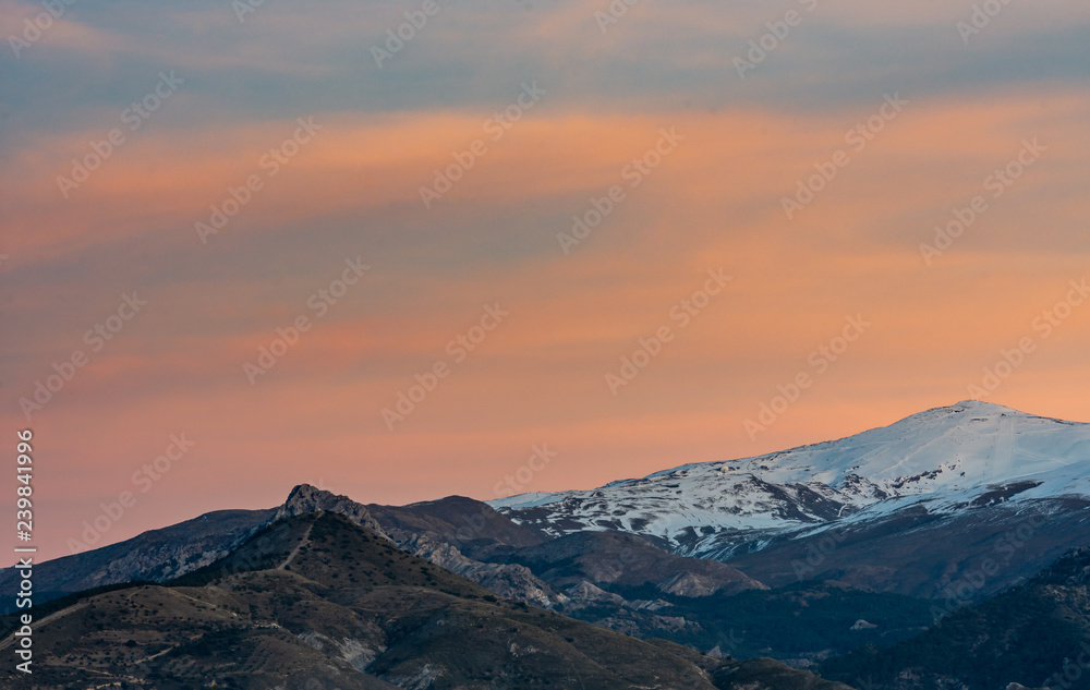 Scenic view of snowcapped mountain El Veleta and Trevenque during sunset with orange tones in the sky, Granada