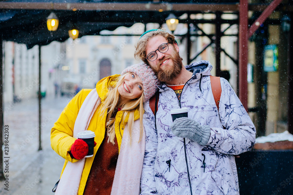 Young excited woman put her head on the shoulder of her boyfriend while walking in cold winter city street. Gentle portrait of hipster traveler couple iin love outdoor.