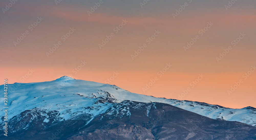 Beautiful scene of snowcapped mountain summit ( El Caballo) in Sierra Nevada during sunset with orange tones on the sky, Spain Beautiful scene of snowcapped mountain summit ( El Caballo) in Sierra Nevada during sunset with orange tones on the sky, Spain