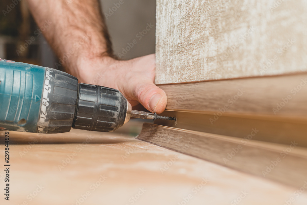 Technology installation and installation of plastic floor plinth - the master with a screwdriver fastens the plinth to the wall