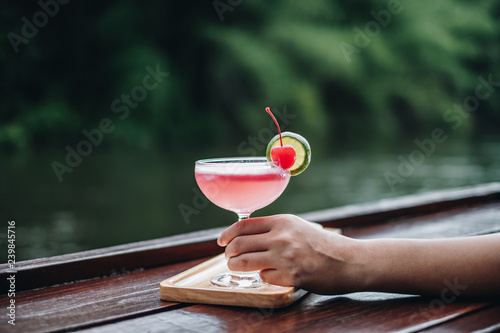 Young woman sitting in outdoor rafting cafe, drinking cocktail and watching the river at sunset. Summer holiday chilling out