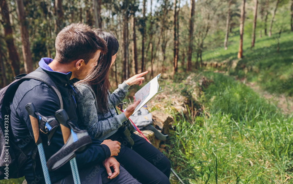 Fototapeta premium Young couple doing trekking sitting looking at a map outdoors